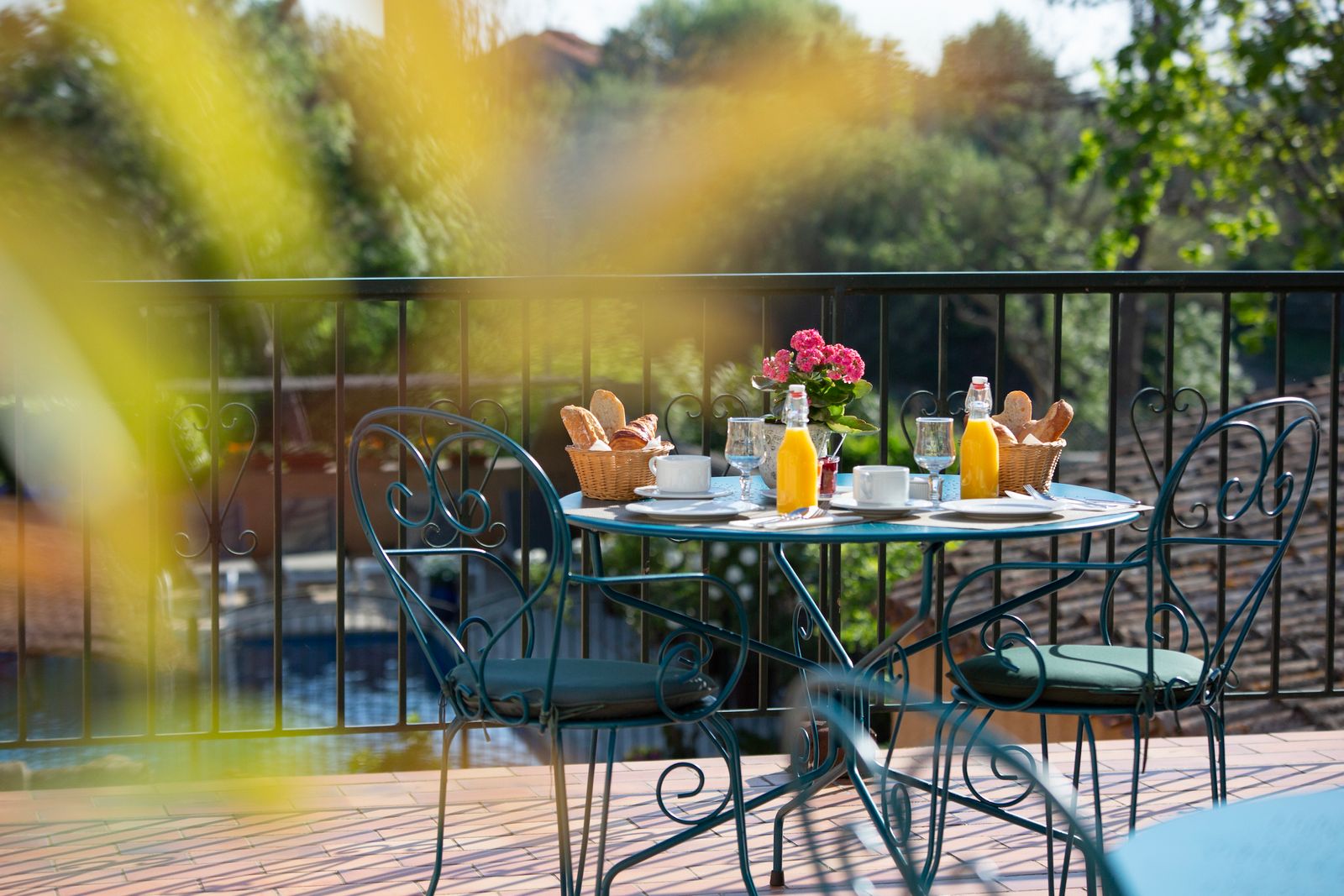 Petit déjeuner sur la terrasse avec boissons chaudes, croissants et jus d'orange, on voit la piscine en arrière plan